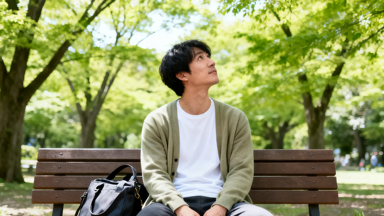 初夏の朝、公園のベンチで木々を眺める男性