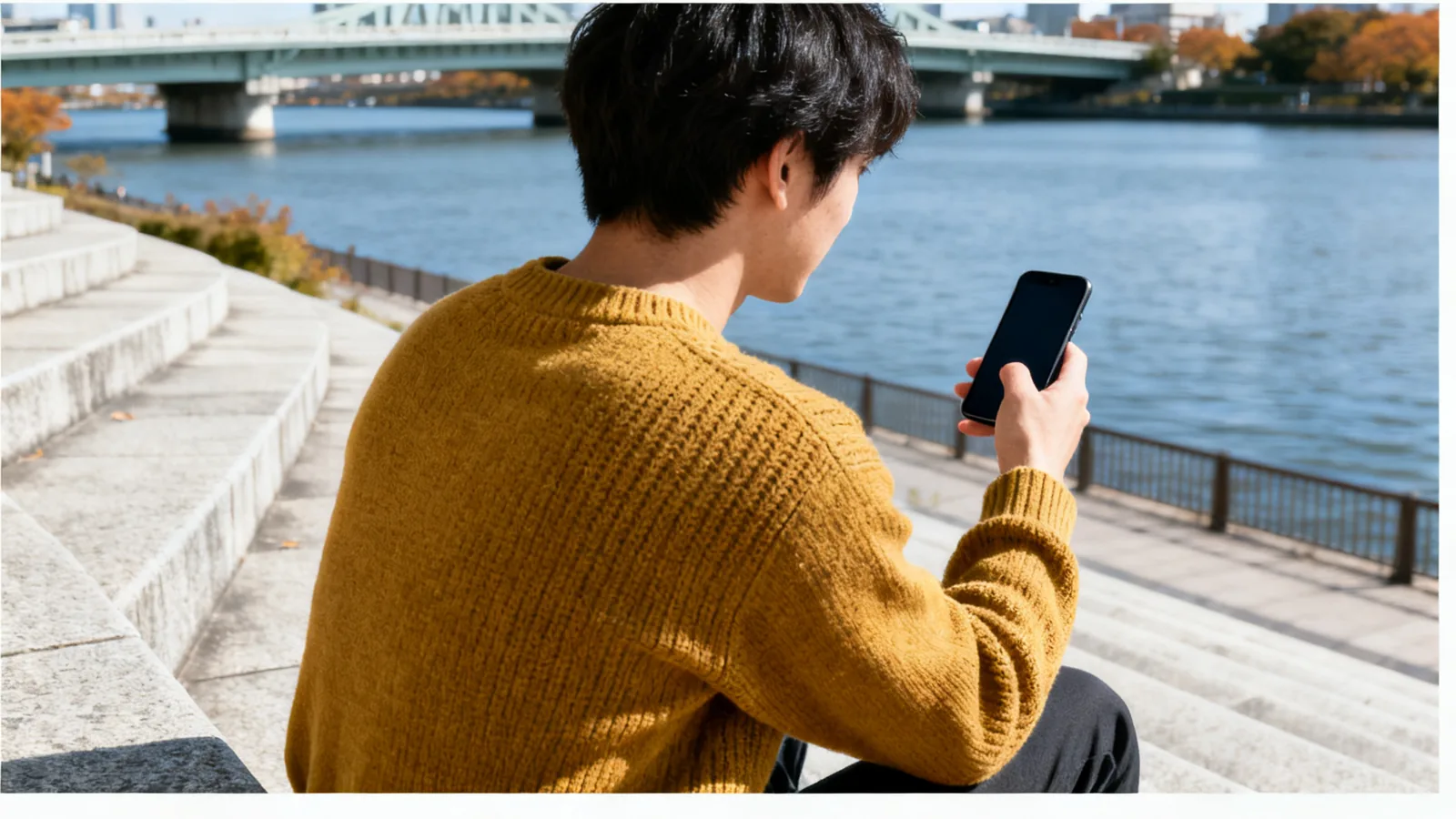 川沿いの石段で、スマホを持ったまま手を止める男性
